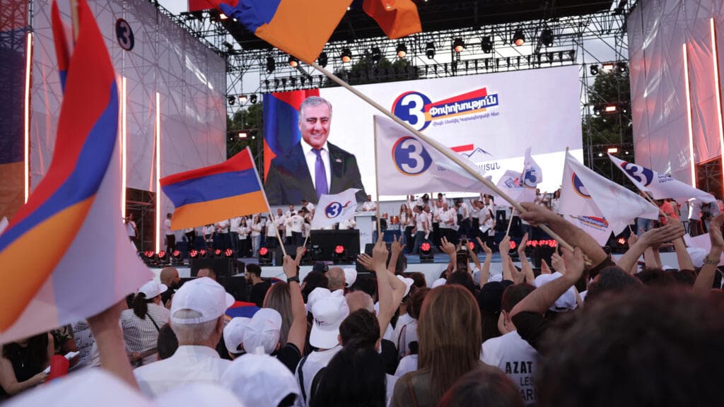 Des partisans du magnat russo-arménien Samvel Karapetyan, à l'écran, participent à un rassemblement avec des drapeaux nationaux arméniens contre le Premier ministre sortant Nikol Pashinian sur la place de la République, à Erevan, en Arménie, le mercredi 3 juin 2026.