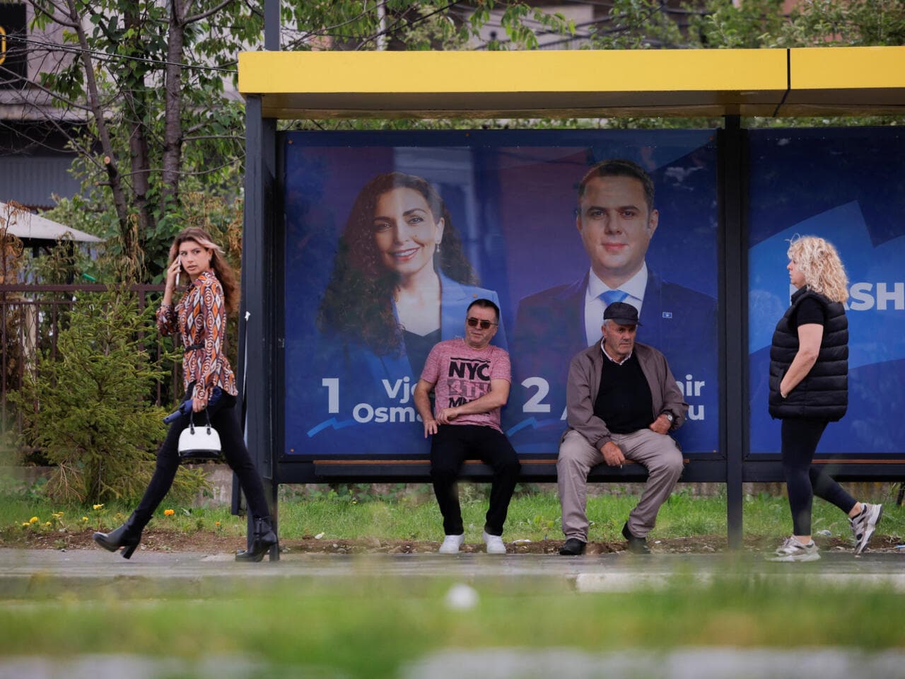 Des personnes attendent à un arrêt de bus près des affiches électorales du parti de la Ligue démocratique du Kosovo (LDK) à Pristina, au Kosovo, le 4 juin 2026.